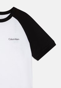 Musta-valkoinen t-paita pyöreällä kaula-aukolla, lyhyillä mustilla hihoilla ja edessä musta "Calvin Klein" -logo. Puuvillakangas, sileä tekstuuri.