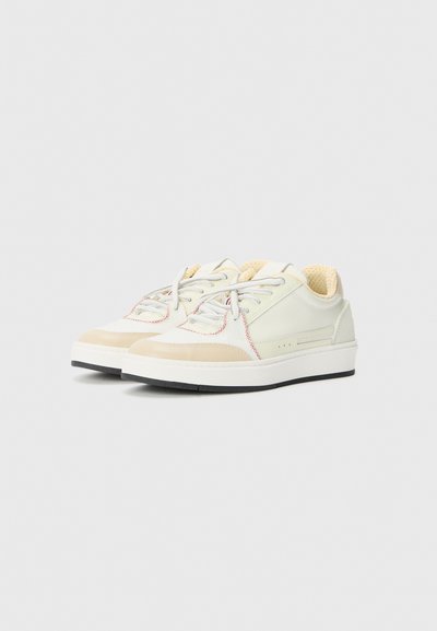 Sneaker di colore chiaro con una combinazione di materiali lisci e testurizzati. Presentano lacci grigi, cuciture rosse a contrasto e una suola in gomma nera.