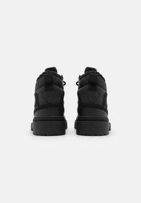 Black ankle boots with padded design, textured fabric, reinforced soles, and black laces. Back includes pull tab and logo detail.