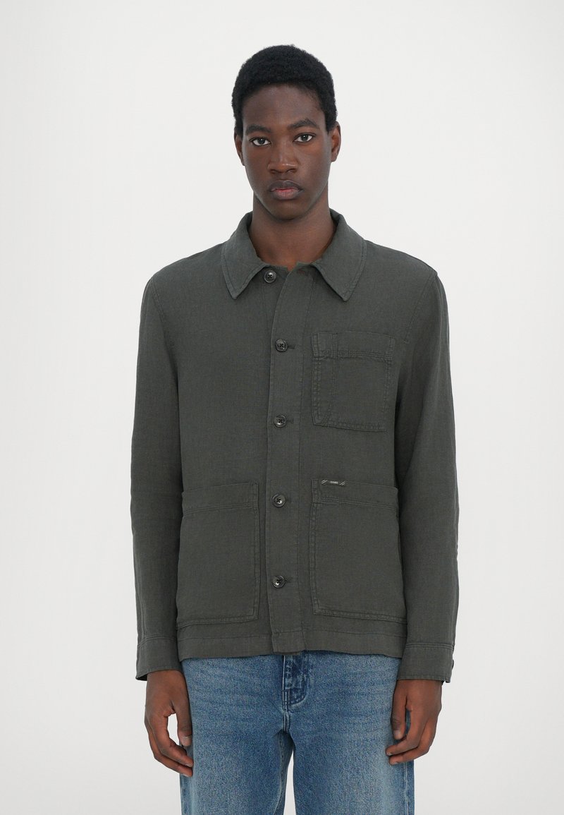 Veste vert foncé en tissu texturé, dotée d'un col, d'une fermeture bouton, d'une poche poitrine et de poches plaquées avec de subtils détails de couture.