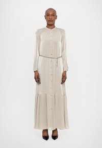 Robe longue en satin beige clair avec un devant à boutons, un col froncé, des manches longues et une jupe à volants. Ceinture en chaîne argentée incluse.