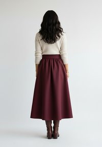 Bordowa spódnica midi z marszczonym pasem, wykonana z gładkiego materiału, zestawiona z brązowymi kozakami za kolano, widziana od tyłu.