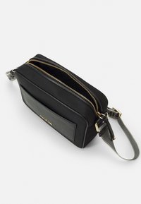 Černá crossbody taška vyrobená z hladkého materiálu, s texturovanou přední kapsou, dvěma zlatými zipy a dekorativním ramenním popruhem s potiskem.