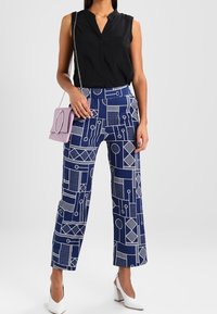 Pantaloni a gamba larga blu navy con motivi geometrici bianchi, abbinati a una maglietta senza maniche nera e a una piccola borsa lavanda. Scarpe con tacco bianche.