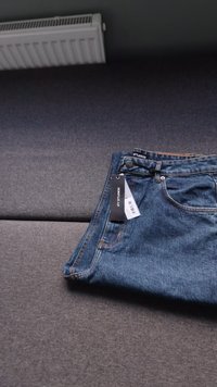 Modre kavbojske hlače z etiketo. Imajo pet žepov, zadrgo in oranžne šive ob šivih. Tkanina ima teksturiran zaključek.