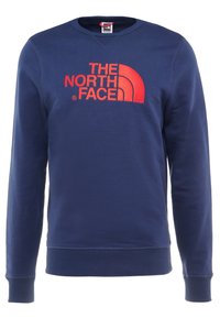 Marinblå sweatshirt med långa ärmar, rund halsringning och ribbade mudd. Har en stor röd logotyp "THE NORTH FACE" över bröstet.