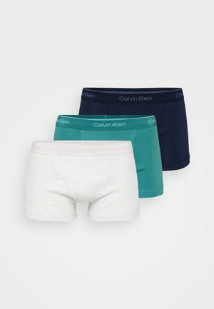 Drie Calvin Klein herenboxershorts in wit, teal en marineblauw, van voren naar achteren gerangschikt op een effen achtergrond.