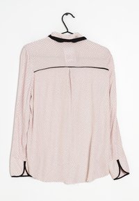 Blusa de manga larga en tejido de color rosa claro con lunares negros, que cuenta con un collar negro, un pliegue en la espalda y un ribete en contraste en los puños.