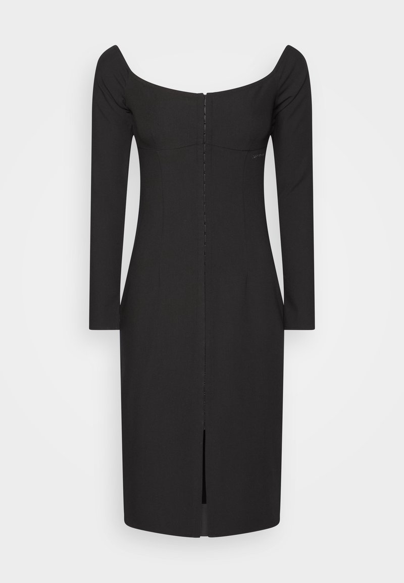 Robe noire ajustée avec décolleté bardot, manches longues et fermeture éclair au dos. Présente un ourlet fendu pour faciliter le mouvement.