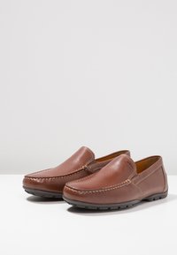 Brune læder slip-on sko med en glat finish, syede detaljer og en rund tå, der har en fleksibel gummisål.