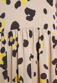 Tissu beige clair avec des taches abstraites noires et jaunes. Présente un détail froncé à l'ourlet, créant une apparence texturée.