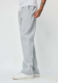 Un pantalon de survêtement gris en tissu doux avec une coupe décontractée, une taille élastique avec cordon de serrage et des poches latérales. Porté avec des baskets blanches.