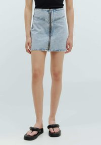 Lichtblauwe denim mini-rok met een voorste ritsluiting, hoge taille en subtiele vervaging. Gepaard met zwarte flip-flops.