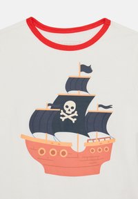 T-shirt bianca con colletto rosso e design di una nave pirata. La nave ha uno scafo rosso, vele nere e un emblema di teschio sulla vela principale.