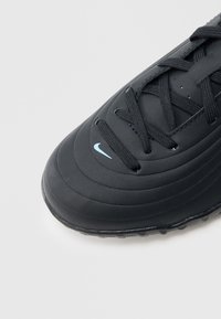 Μαύρο αθλητικό παπούτσι με υφή στο επάνω μέρος, διαθέτει ανεβασμένες γραμμές, μαύρα κορδόνια και ελαφρώς γαλάζιο λογότυπο Nike στη μύτη.