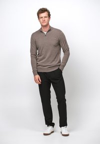 Brauner Zip-Pullover kombiniert mit schwarzen Hosen und weißen Sneakers. Lässiger Schnitt, glatte Textur und minimalistisches Design.