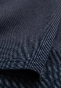 Tessuto blu navy con un motivo testurizzato, caratterizzato da piccoli punti bianchi. Il materiale sembra resistente e ben tessuto, con una finitura liscia.