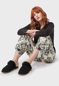 Chaussons en tricot noir avec une bande en fausse fourrure, associés à un haut en dentelle noir et un pantalon crème à motifs avec des designs floraux.