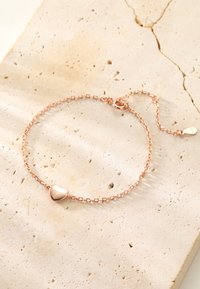 Rose gold bracelet featuring a heart charm, with a delicate chain design and an adjustable clasp on a textured stone surface.