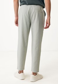 Světlé šedé kalhoty s elastickým pasem a zúženým střihem, s kapsou na zadní straně a hladkou texturovanou tkaninou. Nošeny s bílými teniskami.