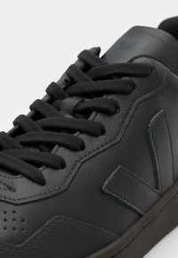 Svart skinn sneakers med svarte snorer, strukturert overflate, subtile sømmer og en fremtredende logo på tungen. Holdbar gummisåle.