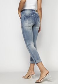 Helle blaue Denim-Jeans mit schmaler Passform, umgeschlagenen Säumen und gestickten Details auf den hinteren Taschen. Kombiniert mit klaren Absatzsandalen.