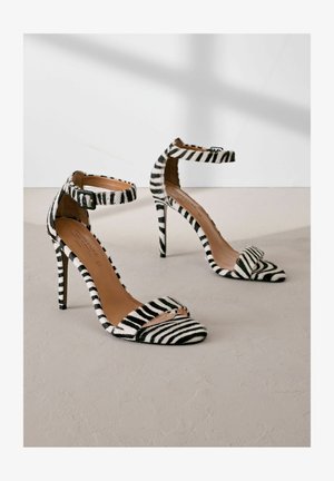 Czarno-białe sandały na wysokim obcasie w paski z odkrytym palcem i paskiem na kostce. Wykonane z miękkiego materiału, z wyprofilowanym noskiem.