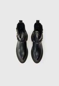 Botas de tornozelo em couro preto com bicos apontados, fivelas decorativas e tachas em forma de estrela sobre um fundo branco liso.