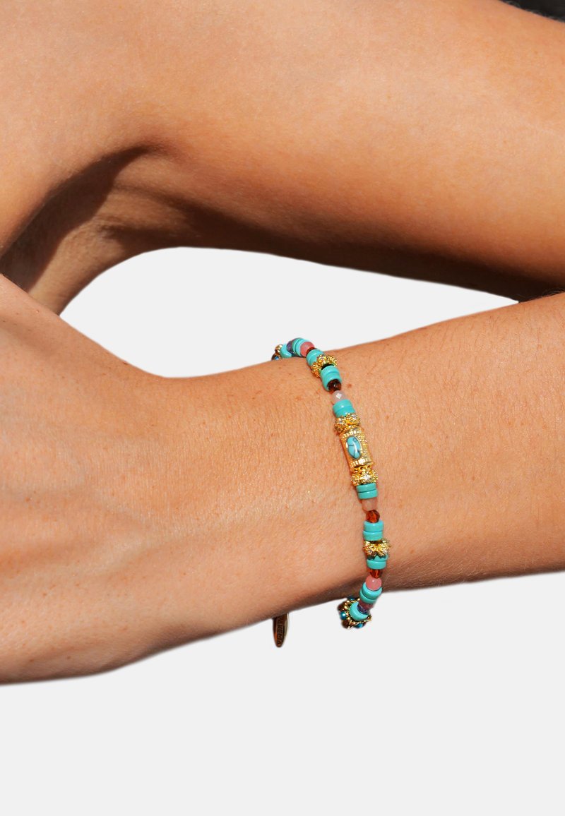 Bracelet coloré en perles avec des accents turquoise, rose et or, présentant des perles texturées, reposant sur un poignet nu.