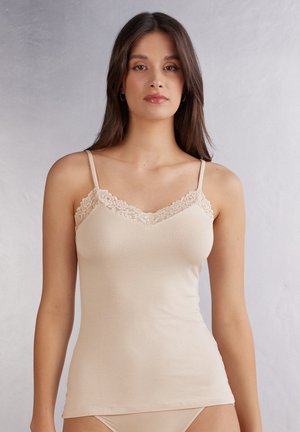 Camisole beige avec dentelle le long de l'encolure et fines bretelles ajustables. Tissu doux avec une coupe ajustée et une texture lisse.