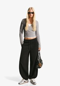 Világosszürke bordázott rövid kardigán gombokkal, fekete laza melegítőnadrág, ezüst sportcipő, és egy fekete kézitáska bunda díszítéssel.