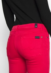 Jeans ajustados de color rosa con una textura suave, que cuentan con bolsillos traseros y una etiqueta de marca en la cinturilla. Construcción estándar de denim.