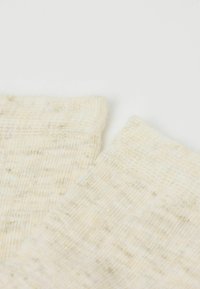 Světle béžové ponožky s metalickými zlatými třpytkami, mírně žebrovaná textura a zakončení manžet. Měkký pletený materiál, všestranný design vhodný pro různé příležitosti.