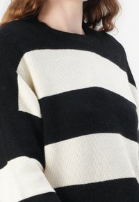 Schwarz-weißer gestreifter Strickpullover mit gerippter Textur und lässiger Passform. Rundhalsausschnitt und weit geschnittene Ärmel.