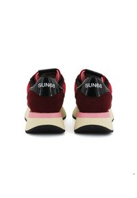 Sneaker rossi e neri con una tomaia in suede, intersuola rosa e branding bianco. Suola nera con battistrada per aderenza e stabilità.