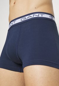 Navy blue boxers made of smooth cotton with a contrasting white branded waistband and visible stitching detail on the leg openings.