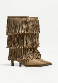 Zamszowe botki w kolorze koniakowym, z warstwowymi frędzlami, zaostrzonymi czubkami i niskimi, blokowymi obcasami. Charakteryzują się gładką teksturą i jednolitym kolorem.