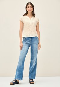 Crème textuur korte mouwen top, gecombineerd met lichtblauwe wijde jeans en marineblauwe sandalen. Eenvoudige, casual outfit met een relaxte pasvorm.