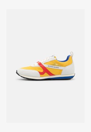 Sneakers with a yellow mesh upper, white suede accents, red side stripes, blue heel tab, and black rubber sole. Branding on the side.
