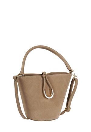 Beige suède bucketbag met gebogen handvat, verstelbare schouderriem en decoratieve goudkleurige metalen ring aan de voorkant.