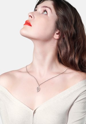 Silberblatt-Anhänger-Halskette an einer zarten Kette, getragen mit einem beige Off-Shoulder-Top; glatte Textur mit filigranen Details auf dem Blatt.