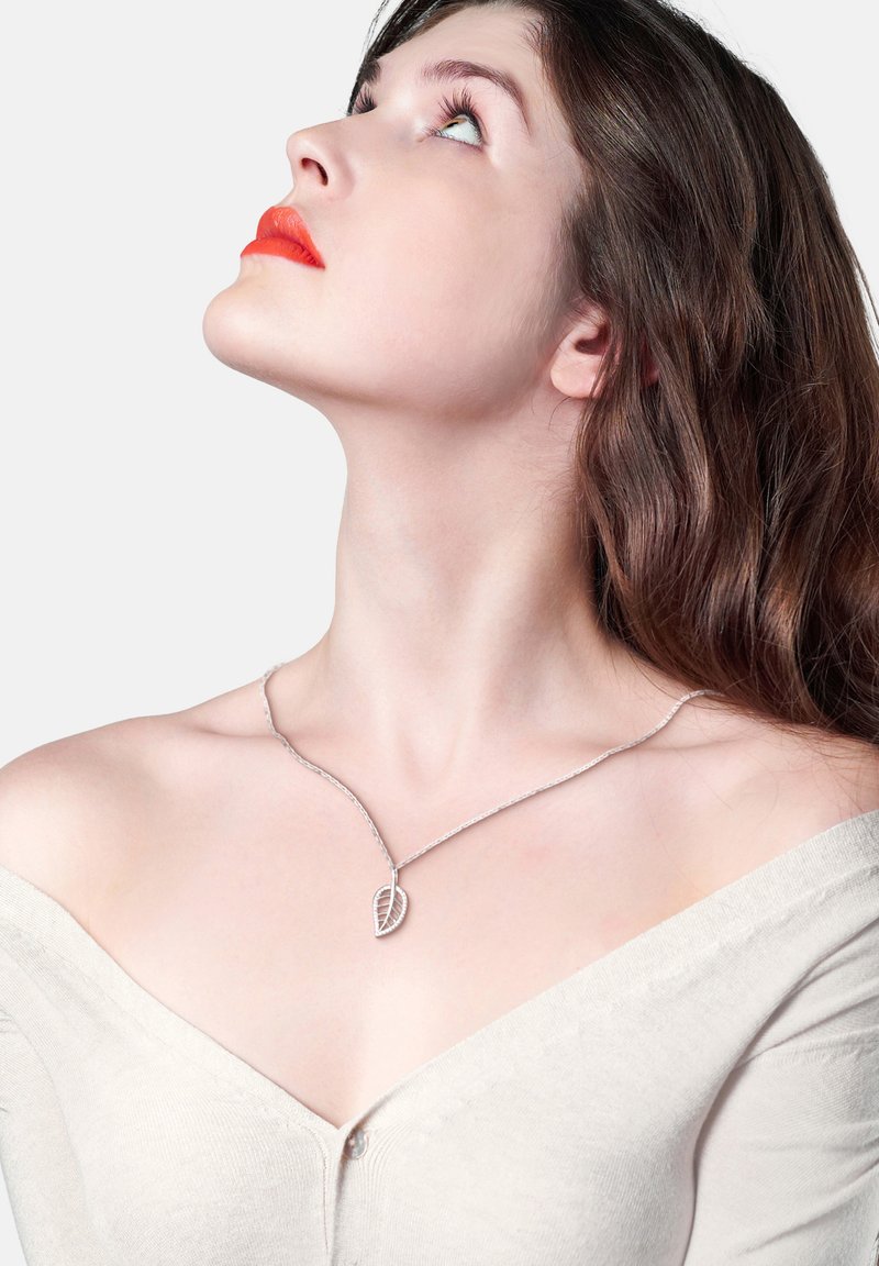 Silverfärgad bladhängsmycke på en delikat kedja, bärs med en off-shoulder beige topp; slät yta med intrikata detaljer på bladet.