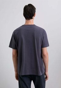 Camiseta gris de manga corta con cuello redondo, hecha de algodón. Presenta un corte relajado y una textura suave. Sin logotipos ni patrones visibles.