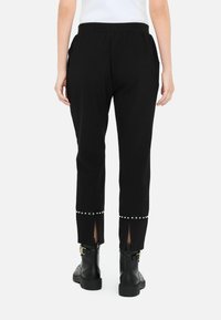 Pantaloni jogger neri con vita elasticizzata, dotati di dettagli con borchie alle caviglie e spacchetti laterali. Abbinati a stivaletti neri.