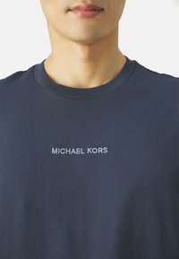 T-shirt in cotone blu navy con collo rotondo, caratterizzato dalla scritta "MICHAEL KORS" ricamata in azzurro sul petto. Texture liscia.