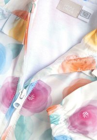 Veste de pluie florale multicolore en tissu léger et brillant. Dotée d'une fermeture à glissière à l'avant et de poignets élastiqués pour un ajustement réglable.