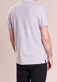 Helles graues Poloshirt mit kurzen Ärmeln, einem Kragen, Seitenschlitzen und kontrastierenden Akzenten am Kragen und den Ärmelsäumen. Aus Baumwollmaterial.