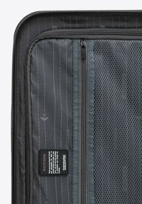 Černý interiér kufru s šedou síťovanou kapsou a zipy. Obsahuje jemný liniový vzor a značkovou nálepku. Texturovaná tkanina, odolný design.