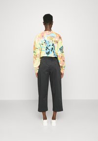 Chemise à manches longues multicolore avec des imprimés graphiques et une coupe décontractée, associée à un pantalon court sombre et des baskets blanches.