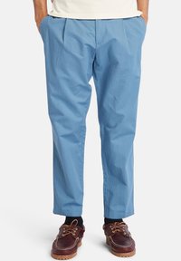 Jasnoniebieskie, plisowane spodnie o luźnym kroju, wykonane z bawełny. W zestawieniu z ciemnobrązowymi butami na sznurowadła i czarnymi skarpetkami.